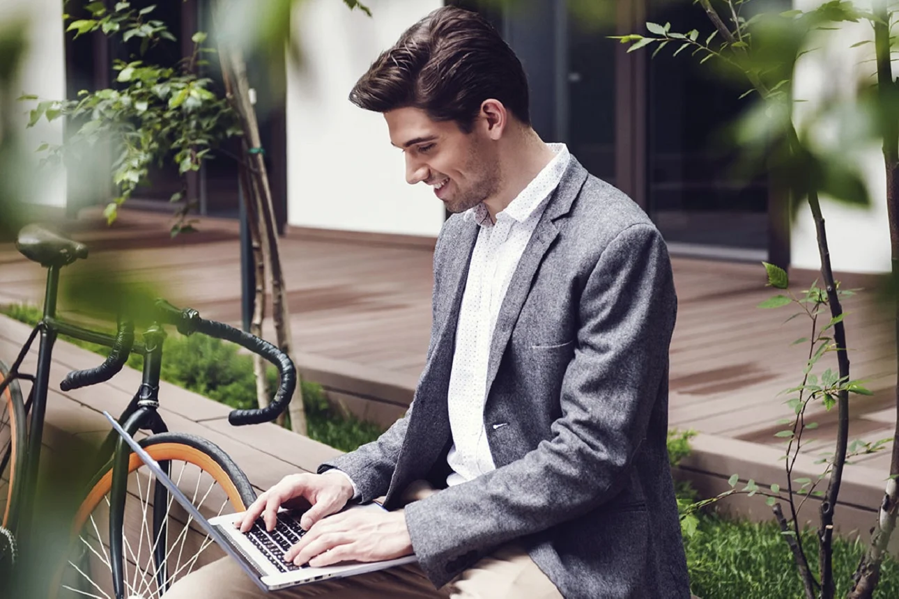 Mann sitzt mit Laptop auf dem Schoß im Garten