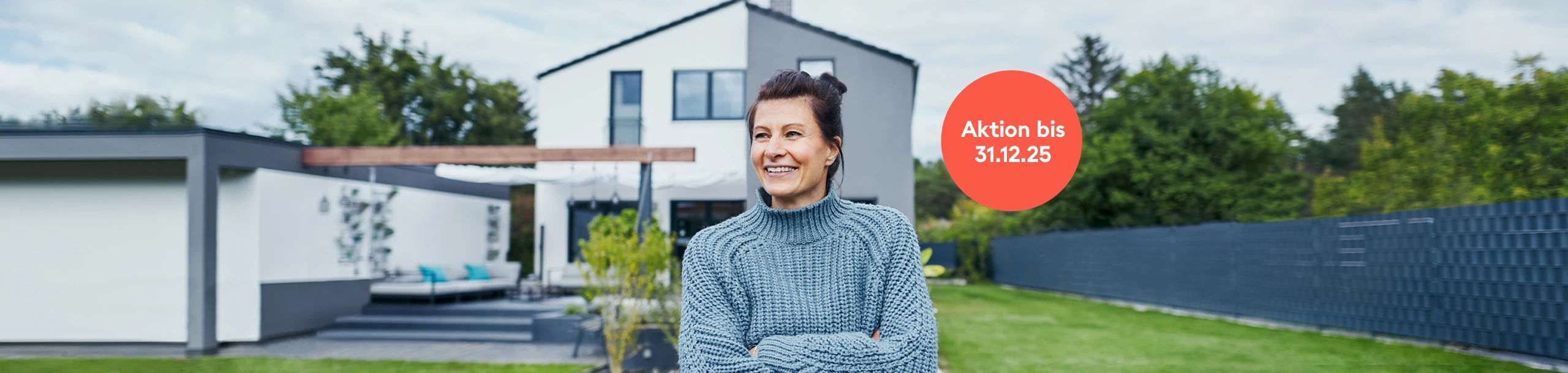 Frau steht im Garten vor Einfamilienhaus und freut sich
