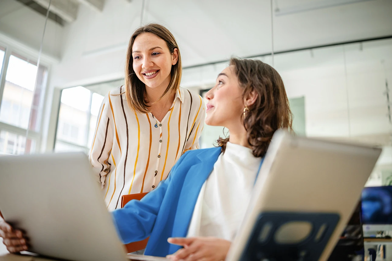 Zwei Frauen arbeiten gemeinsam am Laptop im Büro und lachen