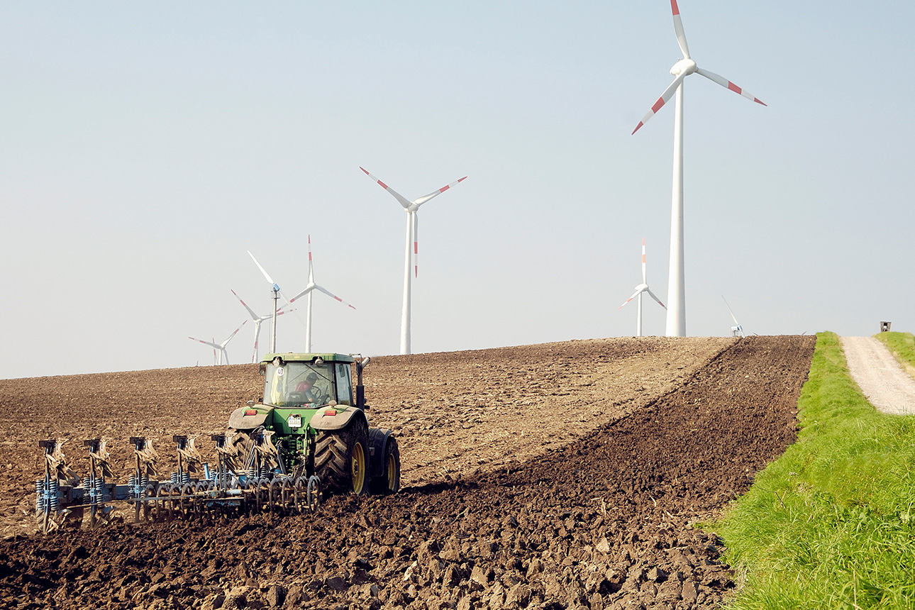 Traktor pflügt Acker, Windkraftanlagen im Hintergrund