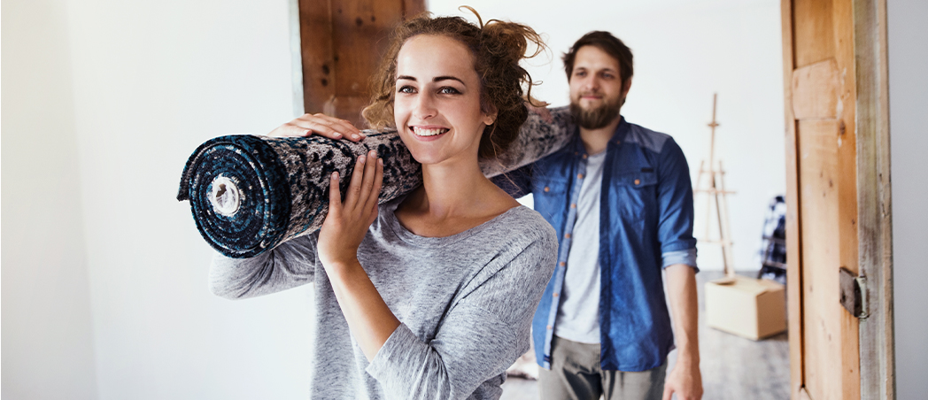 Eine Frau und ein Mann tragen gemeinsam einen Teppich in eine neue Wohnung