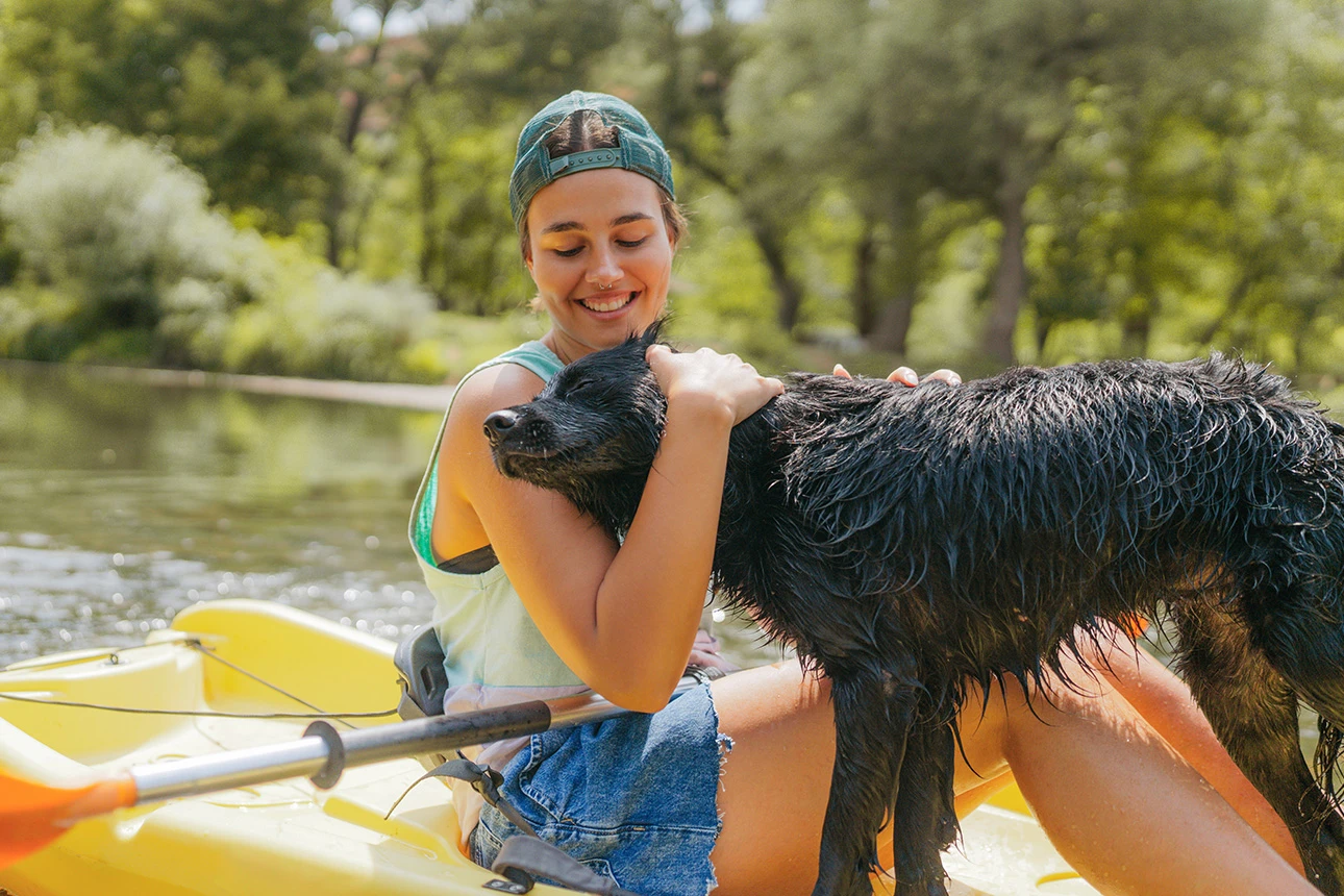 Frau umarmt nassen Hund im Kajak auf einem See