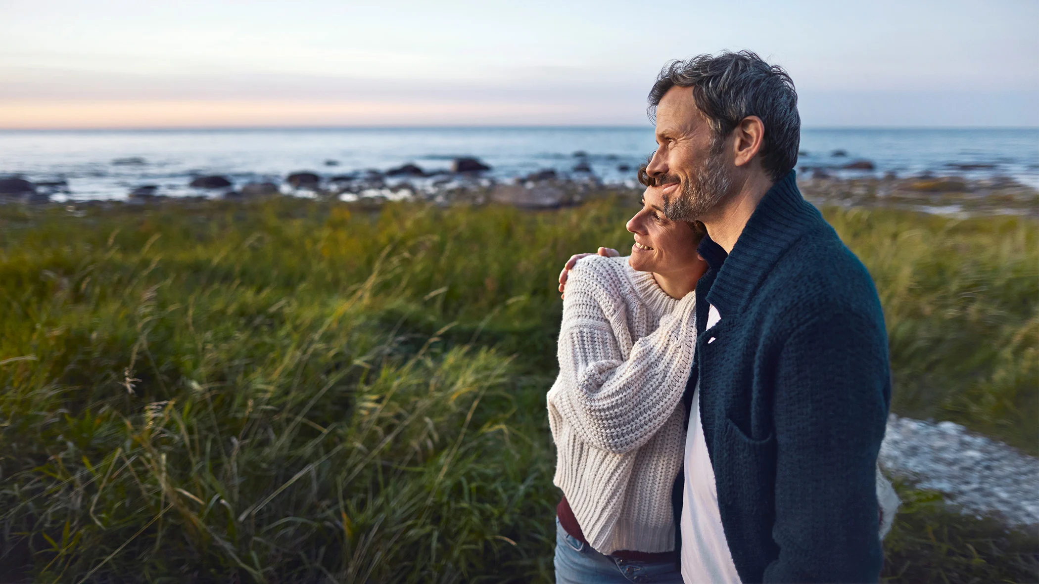 Ein Mann und eine Frau stehen an einem Strand und halten sich im Arm.