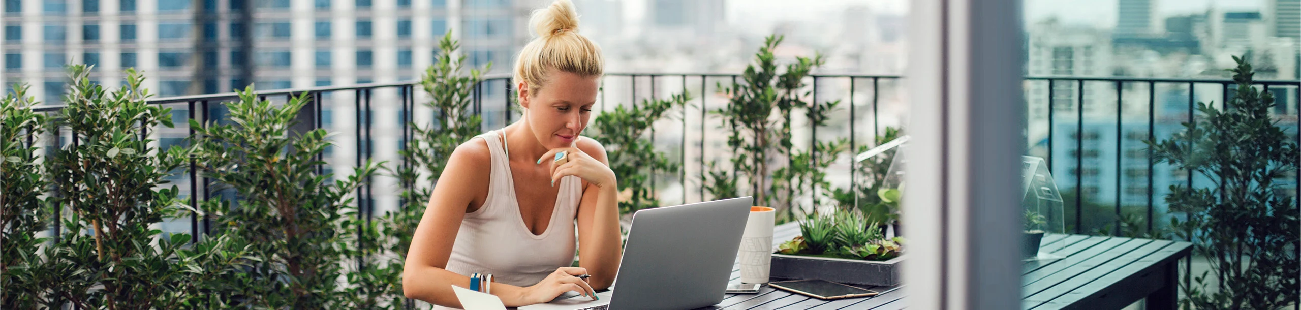 Eine Frau sitzt auf dem Balkon und arbeitet an einem Laptop