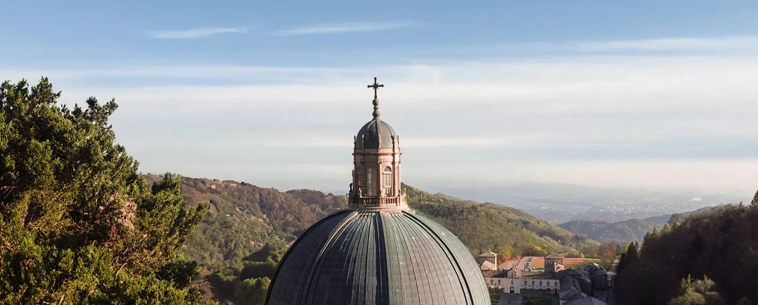 Majestic dome of a church rises above wooded hills under blue sky.