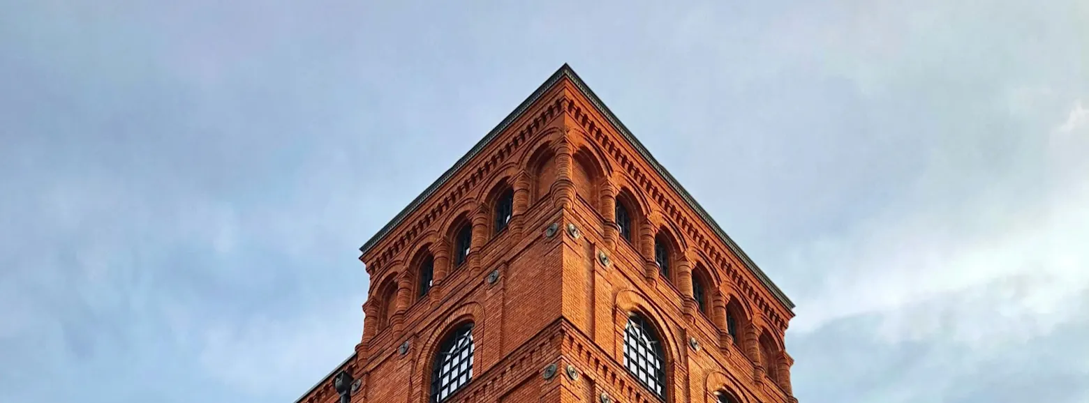A red brick tower with arched windows rises into a cloudy sky. Historic architecture shapes the cityscape.