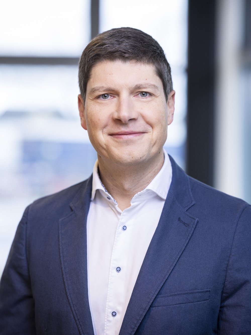 Matthias Wlaka in a blue suit and white shirt smiles warmly at the camera.