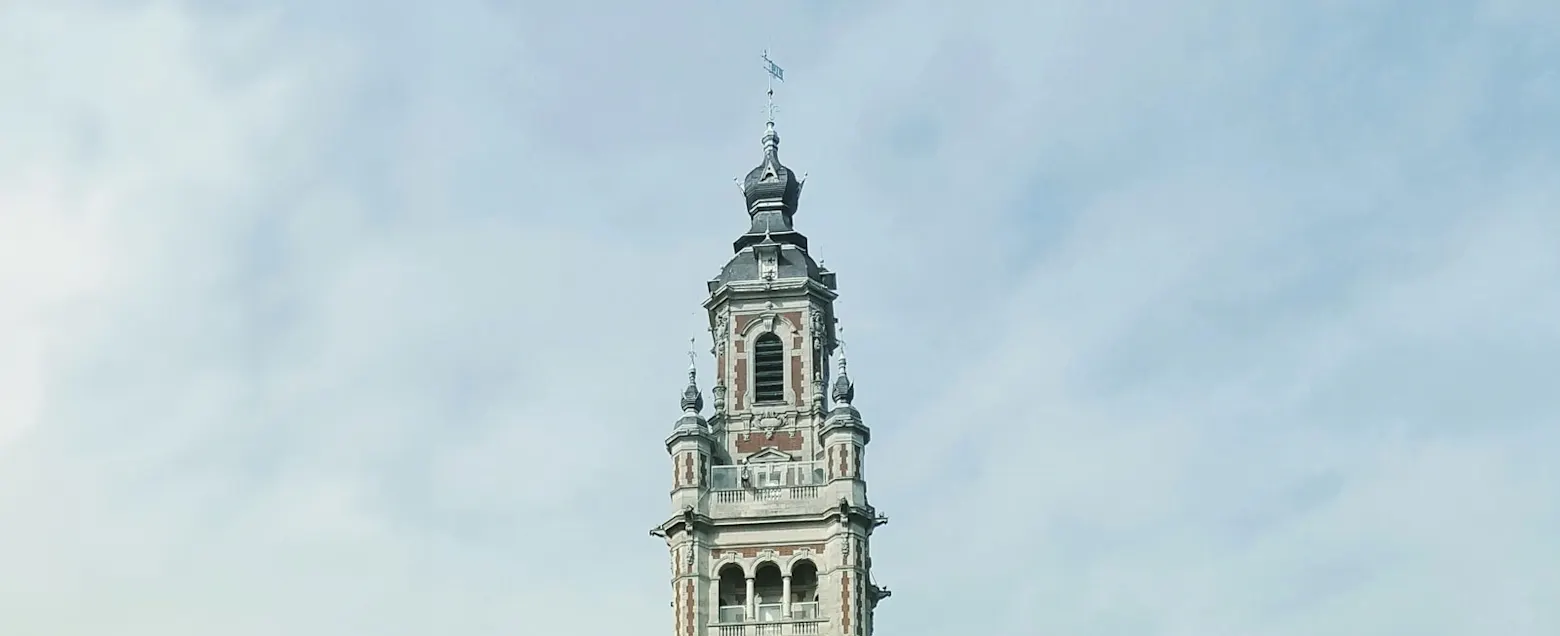 Eleganter Kirchturm ragt in den bewölkten Himmel. Uhr und Glockenturm prägen die Architektur.