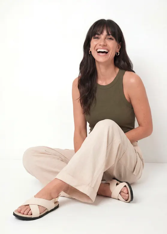 She is wearing an olive-green ribbed top, loose-fitting beige trousers and cream-coloured sandals.