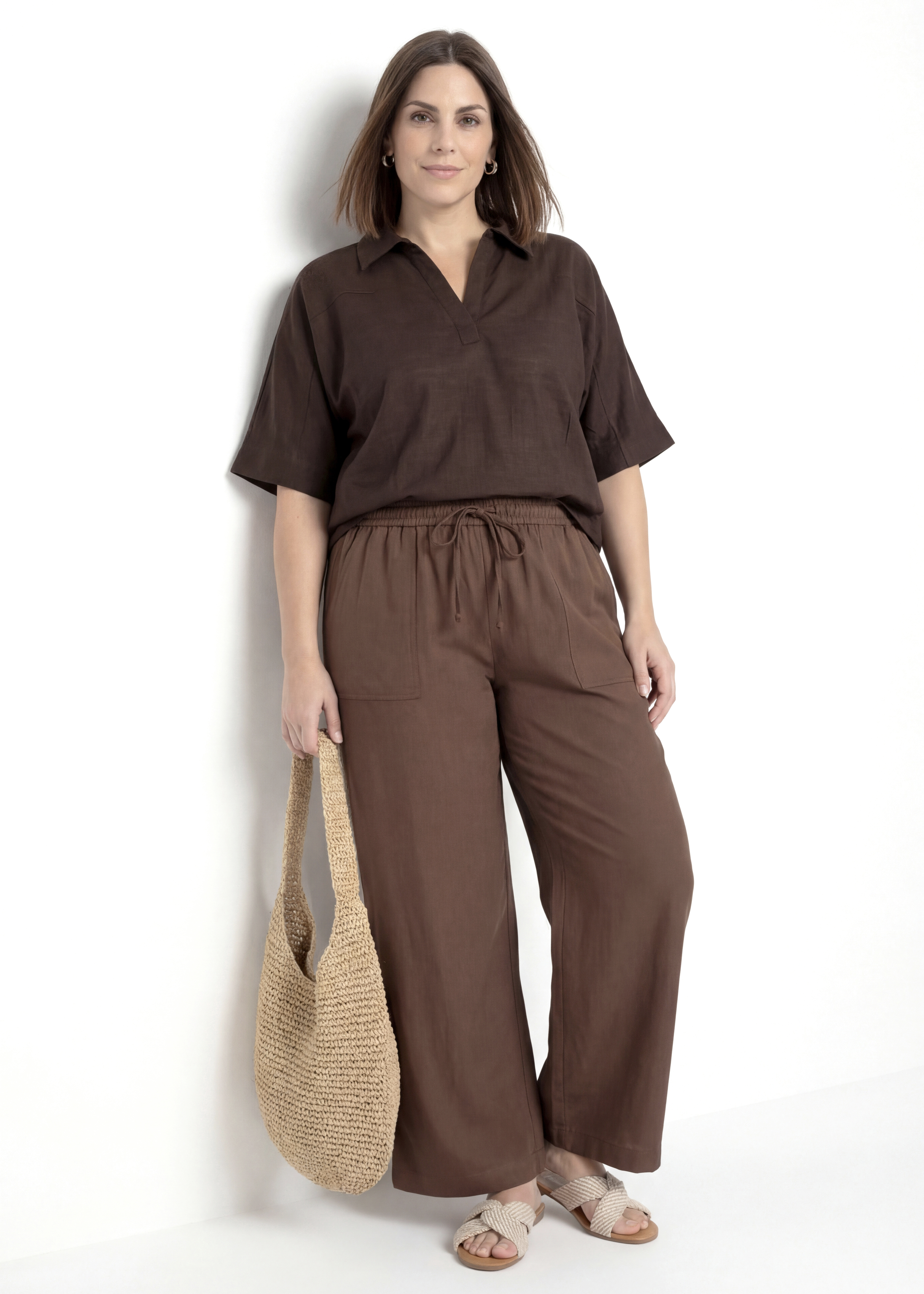 A brown short-sleeved blouse and loose-fitting trousers, paired with beige sandals and a crochet bag.
