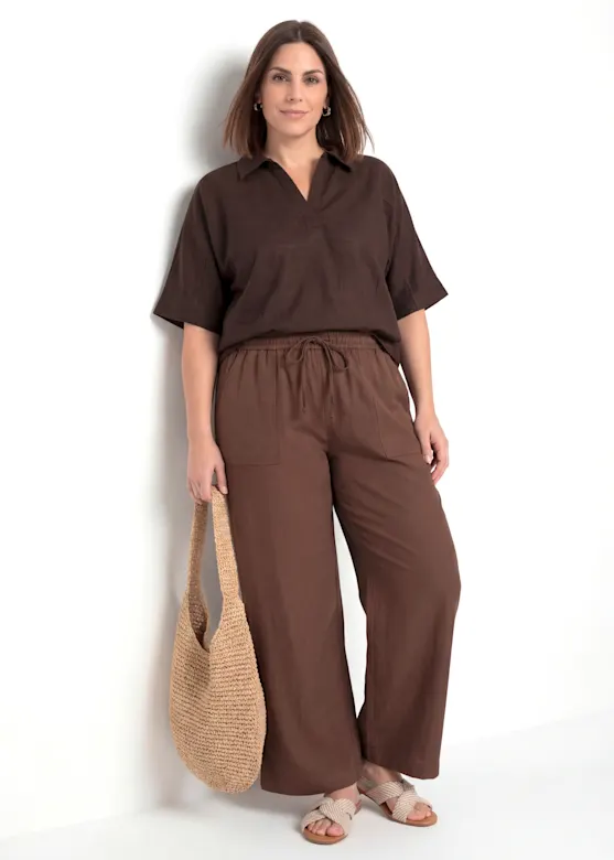 A brown short-sleeved blouse and loose-fitting trousers, paired with beige sandals and a crochet bag.
