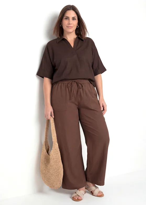 A brown short-sleeved blouse and loose-fitting trousers, paired with beige sandals and a crochet bag.