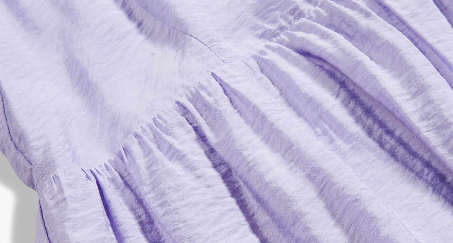 Zarter lila Stoff mit gekräuseltem Saum. Weiche Falten und Texturen im Textil sichtbar.