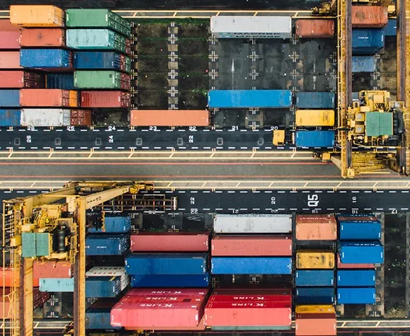 Bunte Frachtcontainer stapeln sich im Hafen. Kräne und Maschinen bewegen die schwere Ladung.