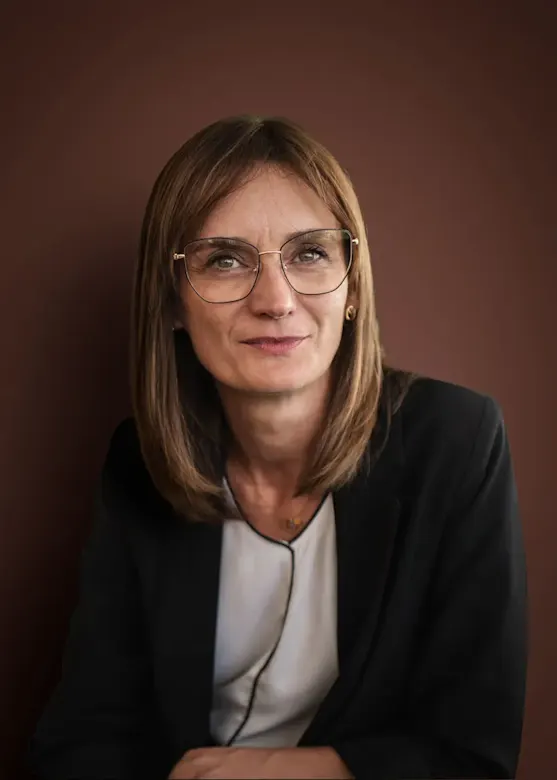 Eine Frau mit braunen Haaren und Brille lächelt freundlich in die Kamera.