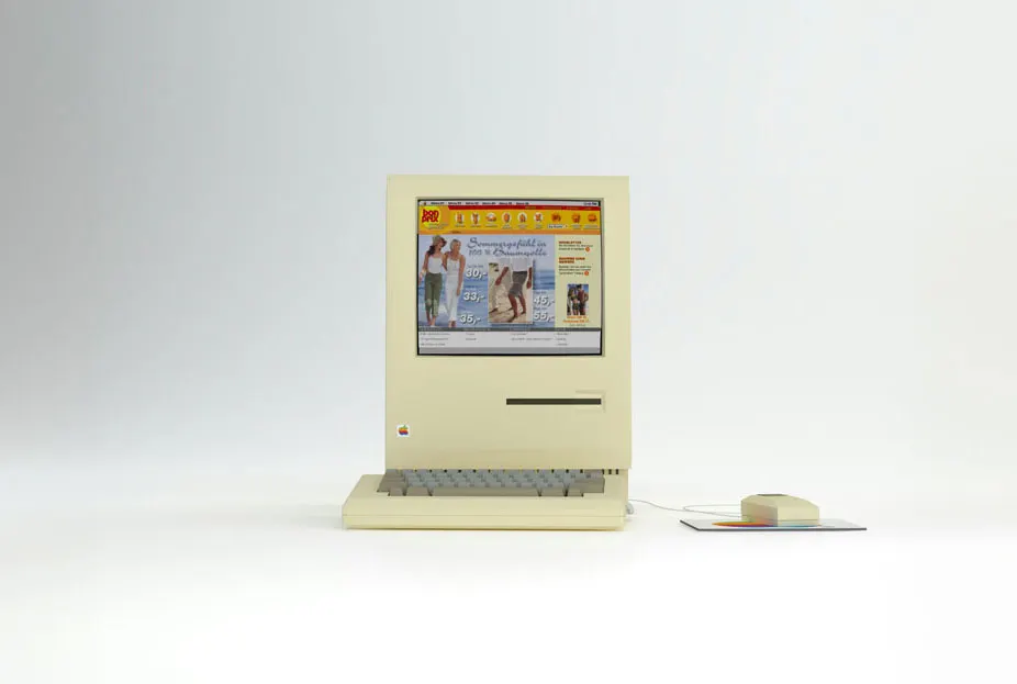 Ein alter Macintosh-Computer mit gelblichem Gehäuse steht auf weißem Hintergrund neben einer Computermaus.