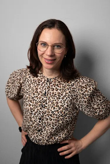 Eine Frau mit Brille und braunen Haaren trägt eine Bluse mit Leopardenmuster.