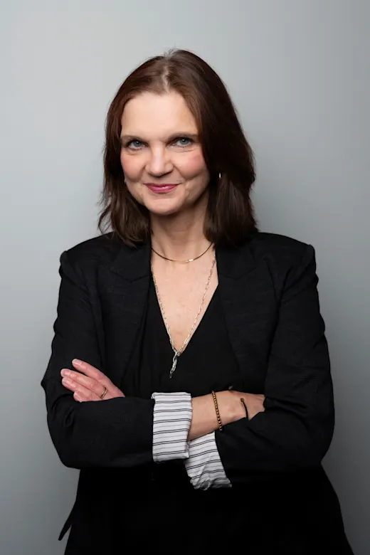 Eine Frau mit braunen Haaren im schwarzen Blazer lächelt freundlich in die Kamera.