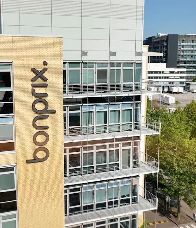 Modernes Gebäude mit gelbem Ziegelstein und "bononx" Schriftzug. Glasfassade und Balkone sichtbar.