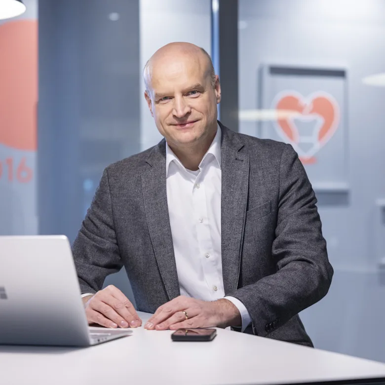 Nicolai Johannsen is wearing a grey-streaked jacket and a light-coloured shirt, and is standing in front of a laptop.
