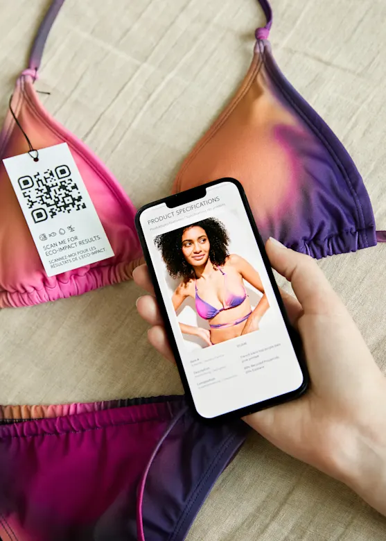 Bunter Bikini mit QR-Code-Etikett neben Smartphone, das eine Frau im Badeanzug zeigt.
