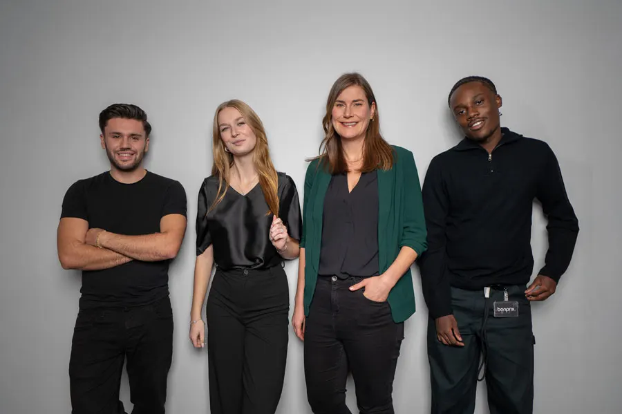 Eine vielfältige Gruppe von vier Personen posiert selbstbewusst vor einem grauen Hintergrund.