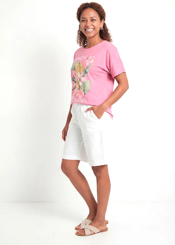 Summer outfit: a pink floral T-shirt, white linen Bermuda shorts and beige mules.