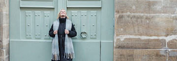 Eleganter Winterlook: Schwarzer Mantel, grauer Schal und Mütze vor mintgrüner Tür.