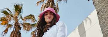 Sommerlicher Look mit weißem Oberteil und auffälligem pinken Hut gegen die Sonne.
