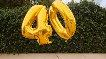 Eine Person in grünem Hemd hält eine alte Sofortbildkamera vor einem hellblauen Hintergrund.