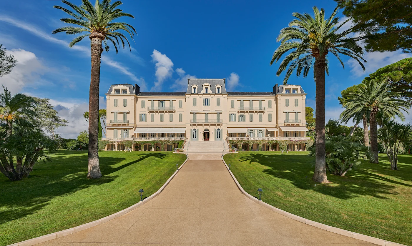The white Napoleon III facade of Hotel du Cap-Eden-Roc between two palm trees