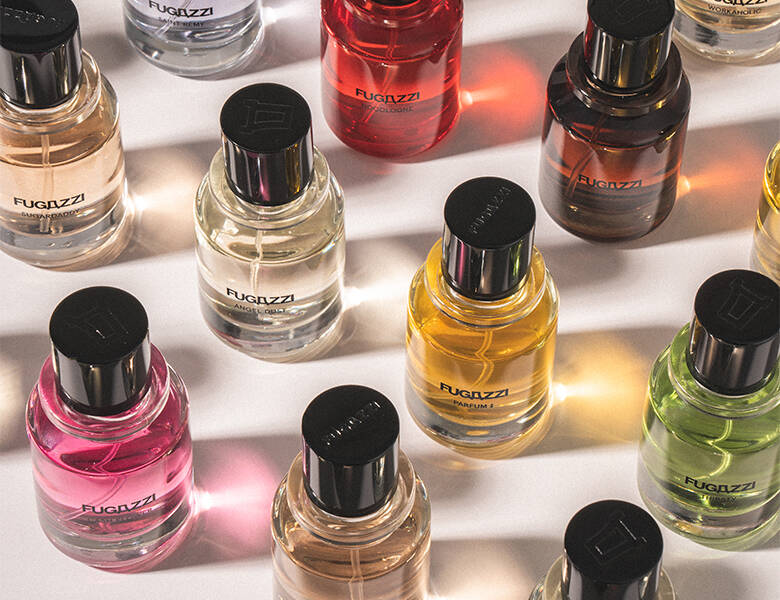 Her ses et hvidt bord, hvorpå der står flere forskellige farverige Fugazzi parfumer med sort låg.