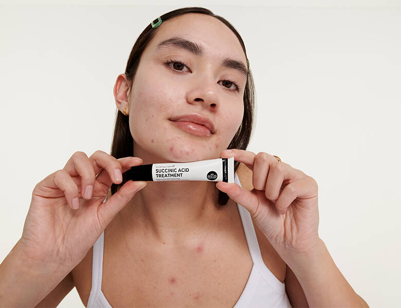 Her ses en hvid baggrund med en kvinde som holder et mindre The INKEY List produkt.