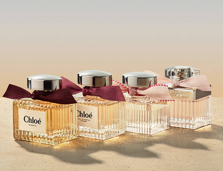 Her ses et billede med fire parfumeflakoner fra Chloé placeret side om side på en lys overflade. Flakonerne er i klare og gyldne nuancer med riflet glas og sølvfarvede låg samt bånd bundet omkring halsen. På nogle af flakonerne står teksten “Chloé”.