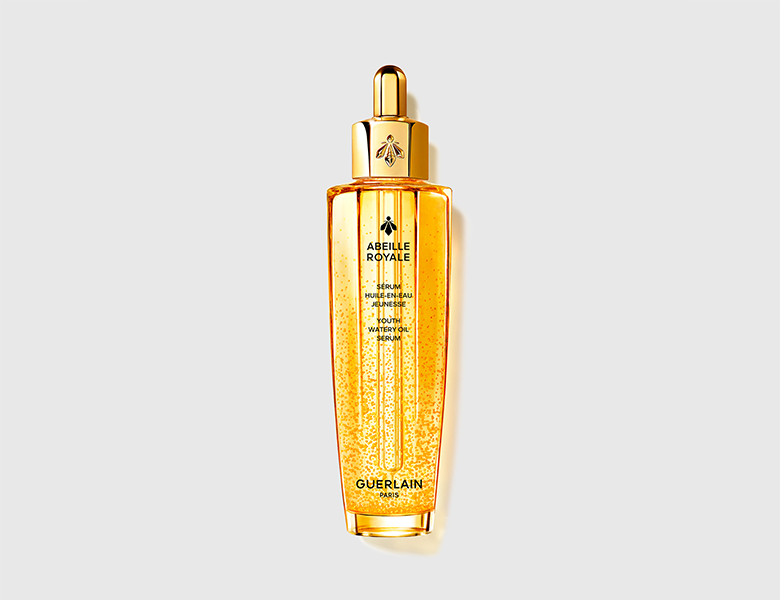 Guerlain Abeille Royale serum i gylden flaske med pipette står centreret på lys grå baggrund.