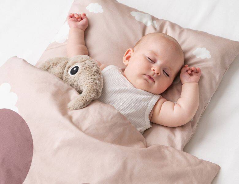 Her ses en sovende baby med sin bamse i sit lyserøde sengetøj. 