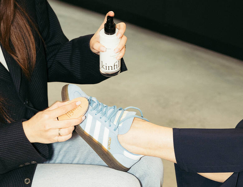 Her ses en kvinde, som er ved at rengøre en anden kvindes blå Adidas sko med to Kinfill produkter. 