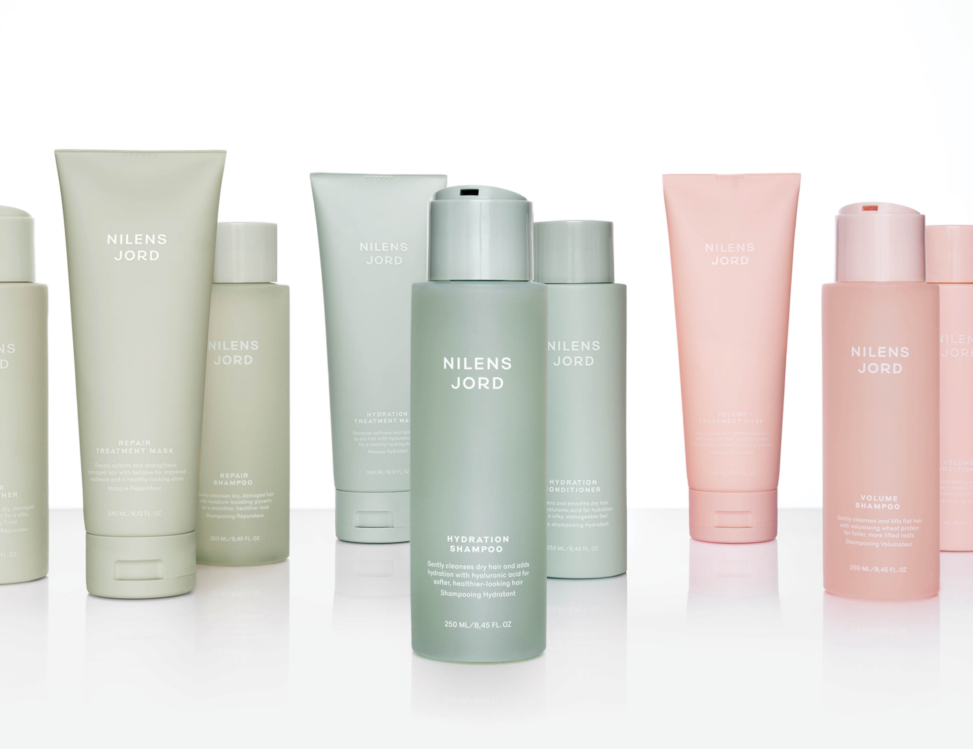 Her ses et billede med flere hårplejeprodukter fra Nilens Jord placeret mod en lys baggrund. Produkterne omfatter blandt andet shampoo, conditioner og hårmasker i grønne og lyserøde nuancer.