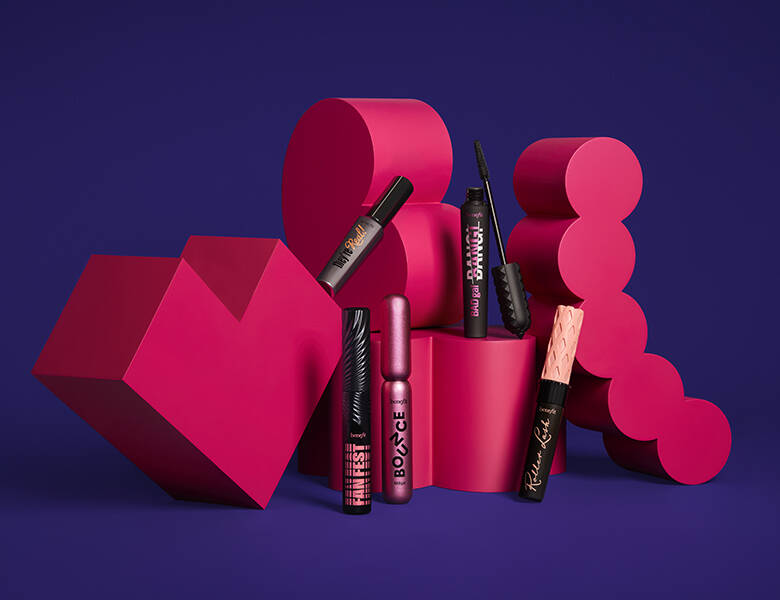 Her ses en mørkelilla baggrund med røde figurer, som fem produkter til øjenvipperne står op af.