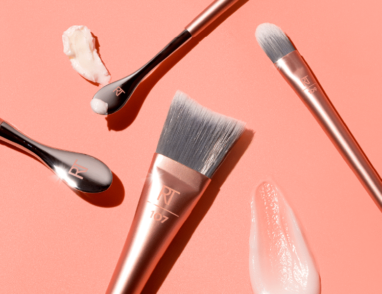 Her ses en laksefarvet baggrund med fire Real Techniques produkter, som kan bruges til hudprep. Ved siden af er der to klatter med hudpleje.