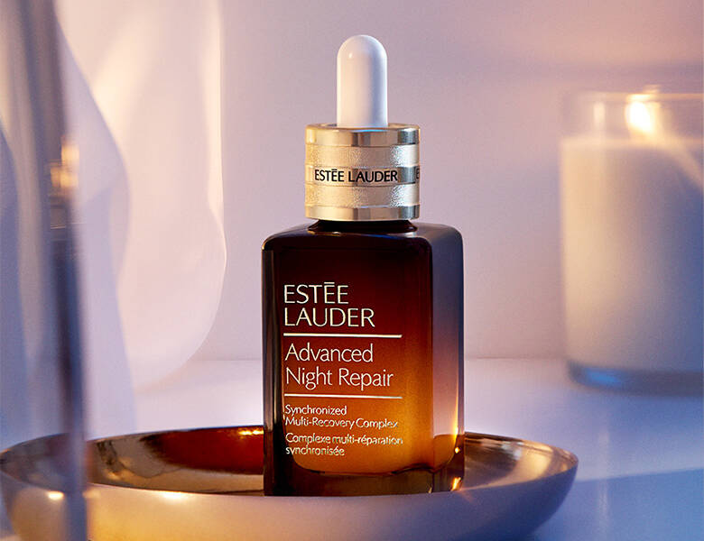 Her ses en Estée Lauder serum på en skål med et levende lys bag sig. 