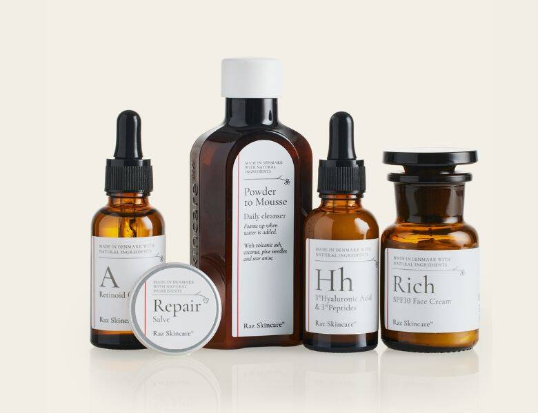 Her ses fem Raz Skincare produkter på en baggrund, som har en meget lysegul farve.