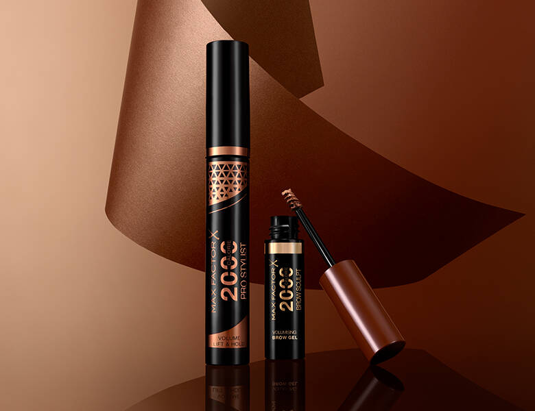 Her ses to øjenprodukter fra Max Factor på en baggrund af flere brune farver og former. 