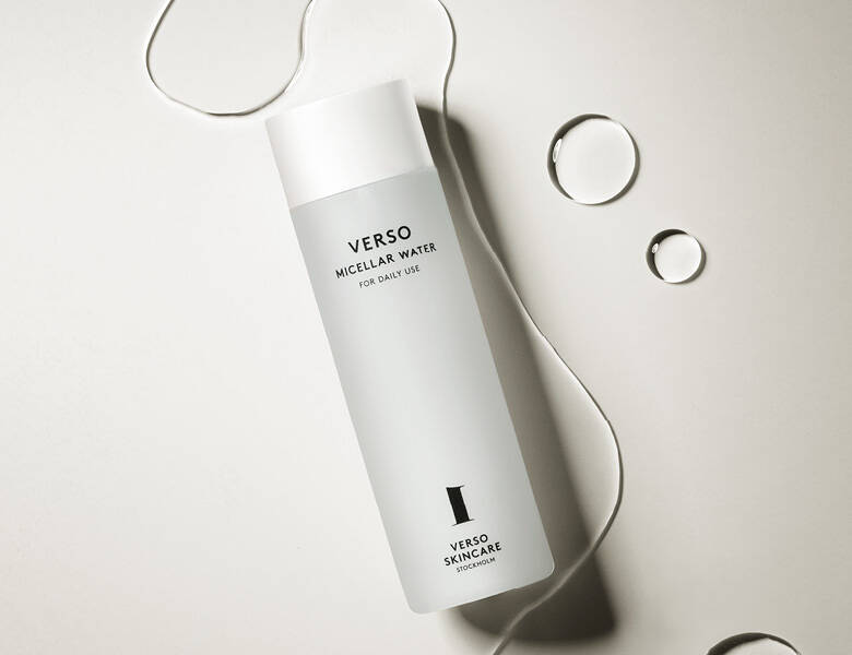 Her ses et Verso produkt med noget klart væske omkring sig. Baggrunden er en lys beige-grå farve.