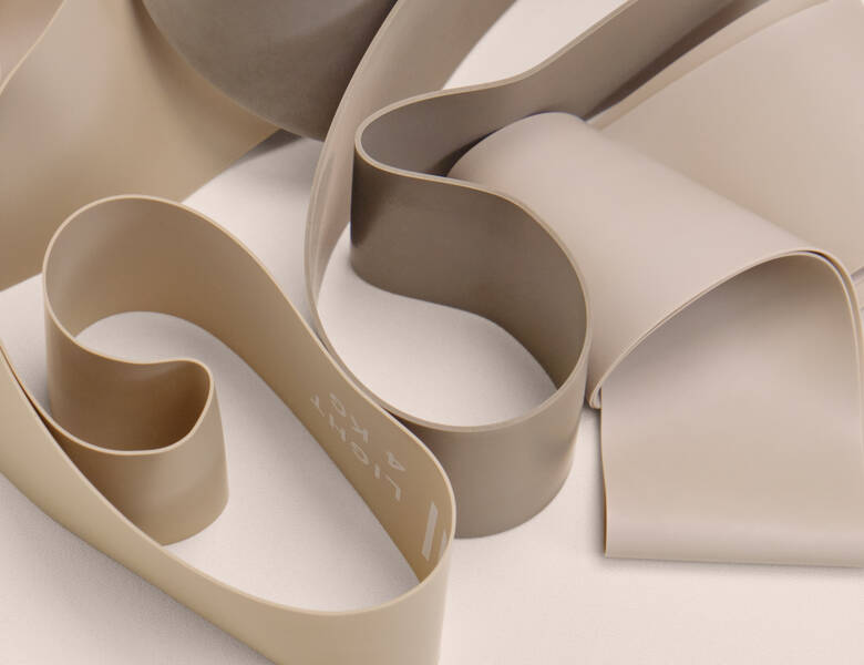 Her ses forskellige beige træningselastikker fra Casall. Baggrunden er lys lyserød.