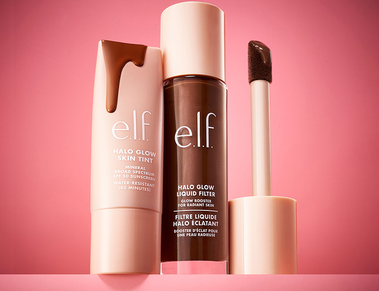 Her ses et billede med makeup-produkter fra e.l.f. placeret mod en pink baggrund. På produkterne står blandt andet “HALO GLOW SKIN TINT” og “HALO GLOW LIQUID FILTER”. Produkterne vises med en applikator med produkt.