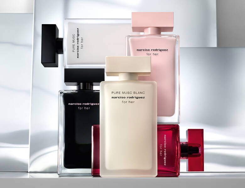 Her ses et billede med flere parfumeflakoner fra narciso rodriguez placeret samlet mod en lys baggrund med spejlende flader. Flakonerne er i forskellige farver, herunder sort, hvid, rosa og rød, og på dem står teksten “narciso rodriguez for her” samt “PURE MUSC BLANC narciso rodriguez for her” på den hvide flakon.