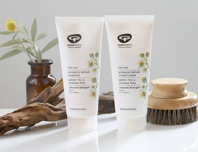 Her ses to hvide og sorte Green People produkter på et hvidt bord med træfarvede dekorationer. 