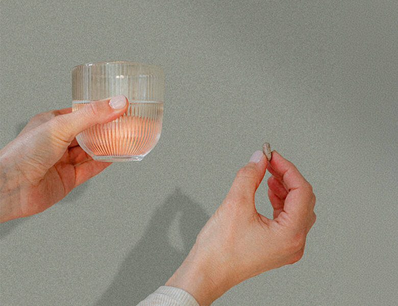 Her ses et sæt hænder, hvor den ene holder en pille og den anden et glas vand. 