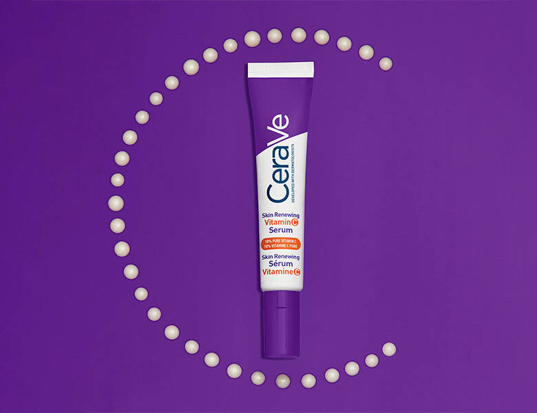 En lilla tube fra CeraVe med teksten “Vitamin C Serum” ligger centreret på en ensfarvet, lilla baggrund. Rundt om tuben er små, ensartede dråber af serum arrangeret i en cirkelform, der danner en dekorativ ramme. Udtrykket er grafisk og farvemættet.